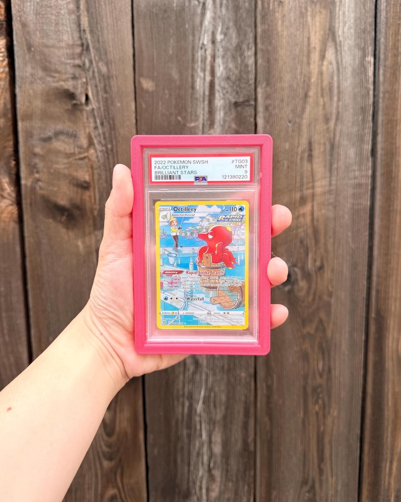 May include: A PSA graded 2022 Pokemon SWSH Brilliant Stars Octillery trading card in a bright pink plastic slab. The card features a red Octillery character in a fishing scene with text including Octillery, Rapid Strike, and 110 HP.