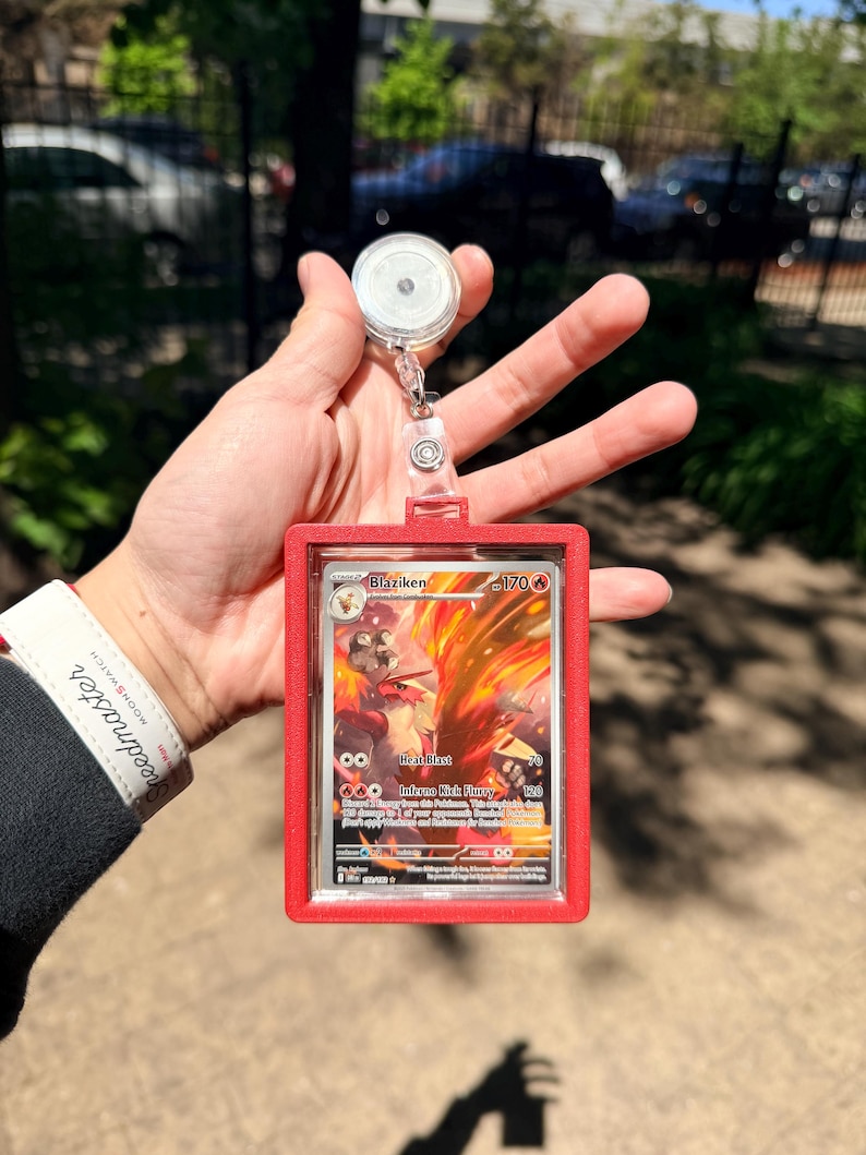 K&ouml;nnte beinhalten: Ein roter Ausweishalter mit einer einziehbaren Rolle, der eine Pok&eacute;mon-Sammelkarte h&auml;lt. Die Karte zeigt eine feurige Illustration von Lohgock mit Text wie "Heat Blast" und "Inferno Kick Fury".