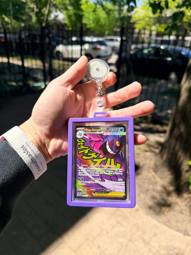 K&ouml;nnte beinhalten: Ein lila Ausweishalter mit einem transparenten Kunststofffenster, der eine Pok&eacute;mon-Karte mit Mega Gengar GX enth&auml;lt. Die Karte hat japanischen Text und farbenfrohe Grafiken. Der Halter ist an einer einziehbaren Rolle mit einem transparenten Kunststoffclip befestigt.