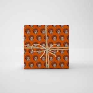 May include: Orange gift wrap with a repeating pattern of a woman's face with curly hair.