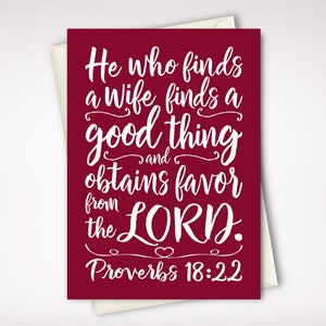 May include: A greeting card with a burgundy background and white script. The text reads "He who finds a wife finds a good thing and obtains favor from the LORD. Proverbs 18:22". The card is inside a cream-colored envelope.