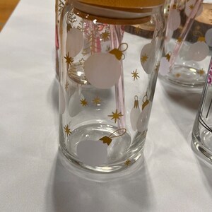 May include: Clear glass tumbler with a bamboo lid, a pink straw, and a gold and white Christmas ornament design. The tumbler is cylindrical and has a capacity of approximately 16 ounces.