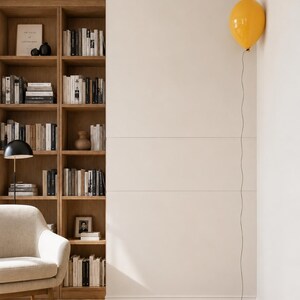 May include: A bright yellow balloon is attached to a thin black string that hangs vertically against a plain white wall. The balloon is positioned in the upper corner of the wall, creating a stark contrast with the neutral, light-colored interior.