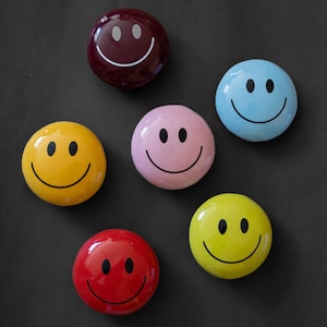 May include: Six smiley face magnets in different colors, including yellow, red, blue, pink, and brown. The magnets are all round and have a simple smiley face design.