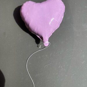 Op de afbeelding: Een paarse hartvormige ballon met een wit touwtje.