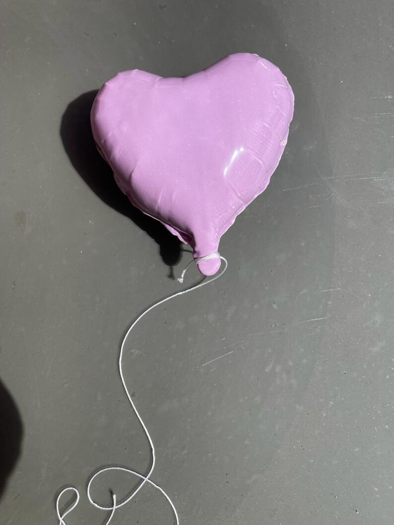 Op de afbeelding: Een paarse hartvormige ballon met een wit touwtje.