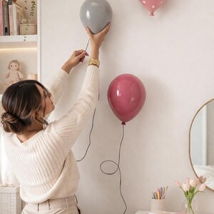 K&ouml;nnte beinhalten: Drei ballonf&ouml;rmige Wanddekorationen. Einer ist grau, ein anderer rosa mit wei&szlig;en Punkten, und der dritte hat eine tiefrosafarbene Farbe. Jeder Ballon hat eine schwarze Schnur. Die Dekorationen sind an einer wei&szlig;en Wand angebracht.