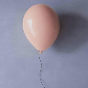 K&ouml;nnte beinhalten: Ein hellrosa Ballon mit gl&auml;nzender Oberfl&auml;che vor einem ged&auml;mpften blauen Hintergrund. Ein d&uuml;nner, schwarzer Faden h&auml;ngt nach unten. Der Ballon ist rund und aufgeblasen. Das Bild hat eine schlichte, klare &Auml;sthetik.