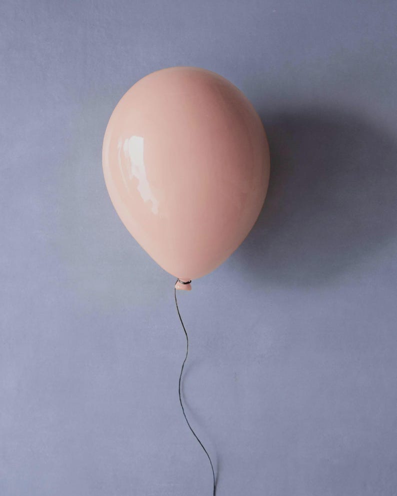 K&ouml;nnte beinhalten: Ein hellrosa Ballon mit gl&auml;nzender Oberfl&auml;che vor einem ged&auml;mpften blauen Hintergrund. Ein d&uuml;nner, schwarzer Faden h&auml;ngt nach unten. Der Ballon ist rund und aufgeblasen. Das Bild hat eine schlichte, klare &Auml;sthetik.