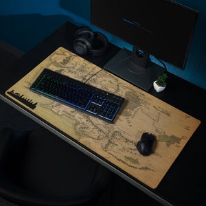 May include: A brown and beige mousepad with a map of Middle-earth from The Lord of the Rings. The map includes the names of various locations, such as Mordor, Rohan, and Gondor. A black keyboard with rainbow lighting and a black mouse are on the mousepad.