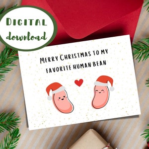 Puede incluir: Una tarjeta blanca con un sobre rojo. La tarjeta tiene un corazón rojo y dos frijoles de dibujos animados con gorros de Papá Noel. El texto de la tarjeta dice "Feliz Navidad a mi frijol humano favorito."