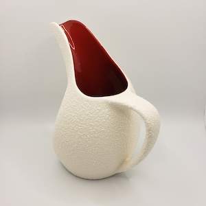 May include: White ceramic jug with a textured surface and a red interior. The jug has a rounded body and a curved handle.