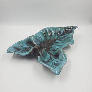 Peut inclure: Un plat de service en céramique en forme de feuille de couleur turquoise et marron. Le plat a une surface texturée et un motif en relief.