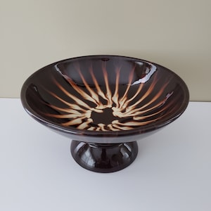 May include: A brown and white ceramic pedestal bowl with a swirl design. The bowl has a wide, shallow base and a tall, slender pedestal.