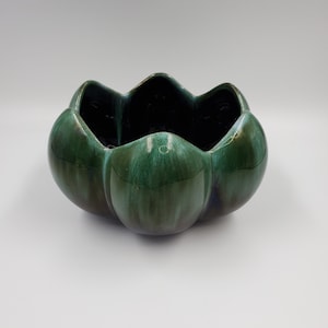 May include: A ceramic bowl with a distinctive petal-like design. The bowl is a deep, glossy green with a dark interior. The exterior has a smooth, rounded shape, and the rim has a scalloped edge. The bowl is likely used for decorative purposes.