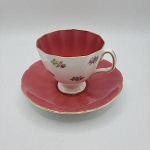 Peut inclure: Une tasse à thé et une soucoupe roses avec un motif floral blanc et une bordure dorée.