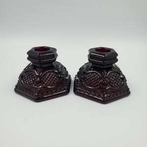 May include: A pair of dark red glass candle holders with a hexagonal base and intricate embossed designs.