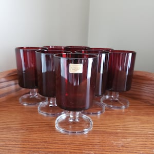 May include: Set of eight red glass wine glasses with clear stems and bases. The glasses have a gold label that reads "Lumero Made in Italy".