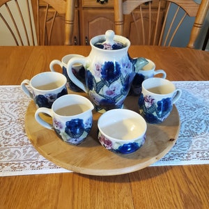 May include: A blue and white floral tea set with a teapot, creamer, and four cups. The set is on a wooden tray with a lace tablecloth underneath.