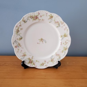 May include: A white porcelain dinner plate with a scalloped edge and a delicate floral pattern in shades of pink and green.
