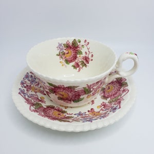 May include: A vintage teacup and saucer set with a floral pattern in shades of pink, purple, and green. The cup has a delicate handle and the saucer has a scalloped edge.
