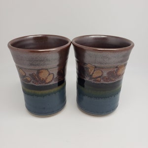 Peut inclure: Deux tasses en céramique brunes et bleues avec un motif floral. Les tasses ont un glaçage brun foncé avec un motif floral brun clair et une base bleu foncé.