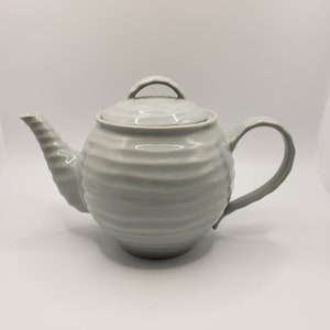 May include: A white ceramic teapot with a ribbed design and a lid. The teapot has a spout and a handle.