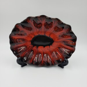 May include: A red and black ceramic bowl with a wavy, flower-like design. The bowl is on a black stand.