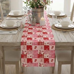 May include: A dining table set for a meal, featuring a red and pink patchwork table runner. The table is set with white plates, bowls, and silverware. A floral arrangement in a metal bucket and a lit candle add to the decor.