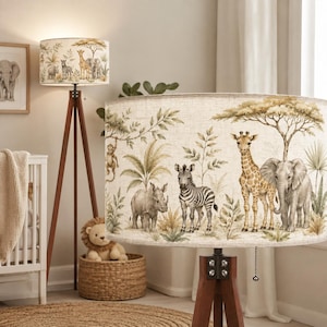 May include: A floor lamp with a tripod wooden base and a cylindrical fabric shade featuring a printed illustration of a monkey, rhinoceros, zebra, giraffe, and elephant among trees and foliage in muted earth tones and soft green accents.