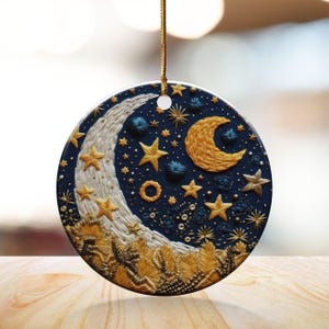 May include: A round ceramic ornament featuring a dark blue background with a textured white crescent moon, a golden yellow crescent moon, and various embroidered-style gold and blue stars. A gold string is attached to the top for hanging.