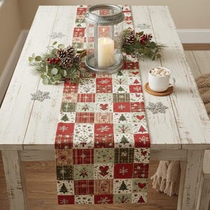 May include: A rectangular table runner featuring a patchwork pattern of red, green, and white squares with holiday motifs including Christmas trees, hearts, and snowflakes. A metal lantern with a white candle sits atop the runner.