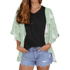 May include: A light green kimono-style top with a white goose and floral pattern. The top has short sleeves and is worn over a black v-neck shirt and denim shorts. The overall style is casual and summery.