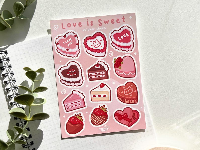 May include: A sticker sheet with a pink background featuring various Valentine's Day themed designs. The sheet includes hearts, cakes, and strawberries, all with a pink and red colour scheme. The text "Love is Sweet" is printed at the top of the sheet.
