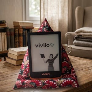 Peut inclure: Une liseuse noire avec une base couleur cuivre posée sur un support en tissu triangulaire. L'écran affiche le texte vivlio et un graphique représentant une personne tenant une tablette. Le support présente un motif répétitif d'éventails rouges et noirs.