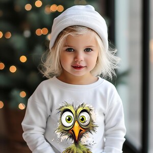 May include: A white long-sleeved sweatshirt with a cartoon green bird with large eyes and a long beak. The bird is wearing a white hat and has a white background.
