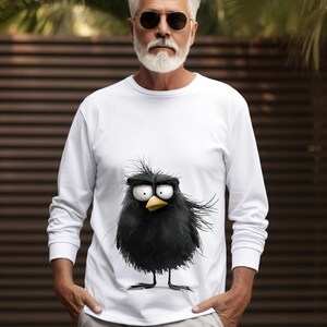 May include: White long-sleeve t-shirt with a cartoon black bird graphic. The bird has a yellow beak and large eyes.