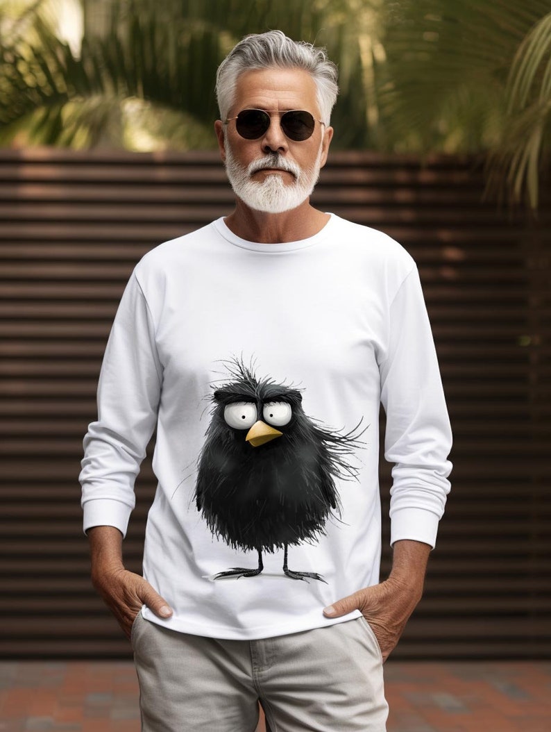 May include: White long-sleeve t-shirt with a cartoon black bird graphic. The bird has a yellow beak and large eyes.