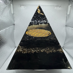 Könnte beinhalten: Schwarze Pyramide mit einem goldenen geometrischen Design und schwarzen Steinen im Inneren. Die Pyramide ist aus Harz und etwa 15 cm hoch.