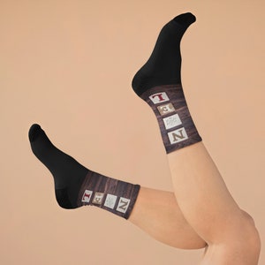 May include: Black socks with a wooden design on the calf area. The design includes the word "ZEN" spelled out with individual letter blocks and a snowflake symbol. The socks are displayed on a person's legs.