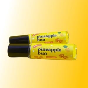 May include: Two yellow and black roll-on perfume bottles with a pineapple bun design. The label says "pineapple bun perfume oil".