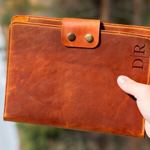 May include: A brown leather folder with a flap closure and two brass snaps. The folder has the initials "D|R" embossed on the front.