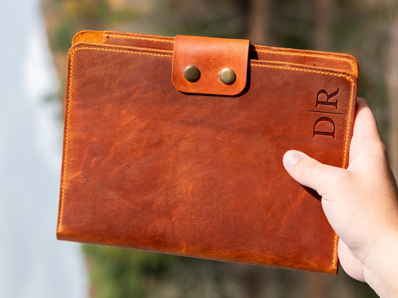 May include: A brown leather folder with a flap closure and two brass snaps. The folder has the initials "D|R" embossed on the front.
