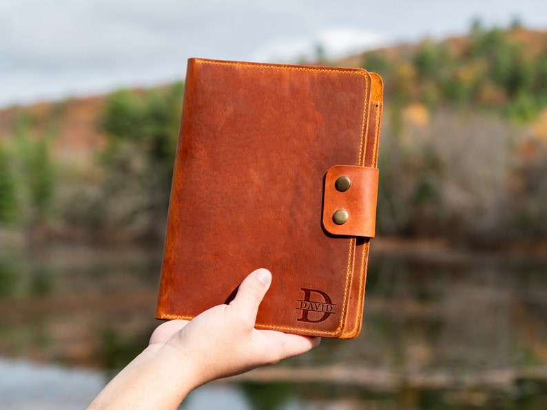 May include: A brown leather journal with a flap closure and a brass button. The journal is personalized with the name "David" in a monogram style.
