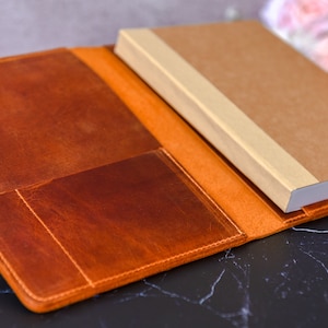May include: A brown leather notebook cover with multiple pockets and a beige notebook inside.