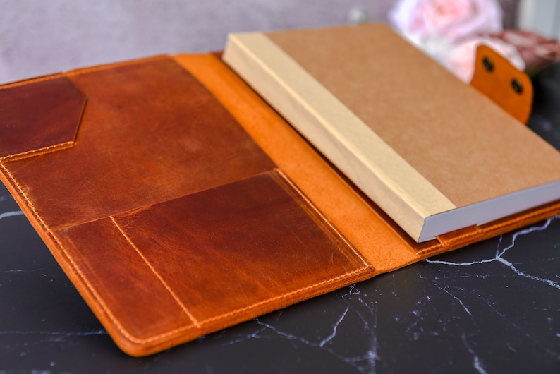May include: A brown leather notebook cover with multiple pockets and a beige notebook inside.