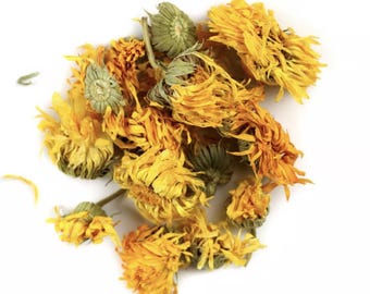 May include: Dried calendula flowers, a vibrant yellow and orange colour, with some green stems and leaves. The flowers are loose and scattered on a white background.