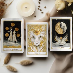 May include: Three tarot cards with gold and white designs are displayed, including "Five of Pentacles", "Strength", and "The Moon". The cards are arranged with candles, dried flowers, and white roses on a neutral-toned surface. The cards have gold borders.