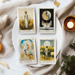 May include: Four tarot cards with gold trim are displayed on a white plate. The cards feature illustrations of the King of Wands, The Moon, Light of Wands, and Page of Pentacles. The cards are surrounded by candles and decorative elements.