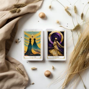 May include: Two tarot cards, "Ten of Cups" and "The World", with gold and white borders. The "Ten of Cups" card features two figures in flowing robes. The "The World" card depicts a figure in a flowing gown. The cards are on a white surface.